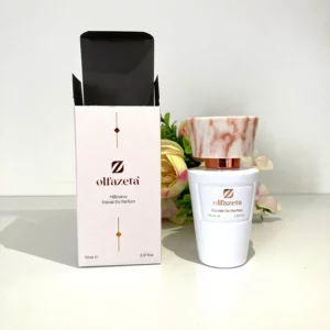 Flacon de parfum Olfazeta Millésime Extrait de Parfum 70 ml avec bouchon effet marbre rose, présenté à côté de son étui élégant blanc et doré, sur fond clair avec décoration florale