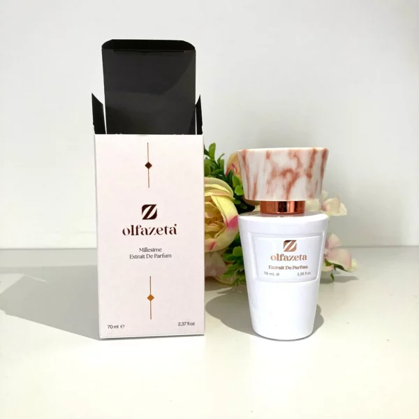 Flacon de parfum Olfazeta Millésime Extrait de Parfum 70 ml avec bouchon effet marbre rose, présenté à côté de son étui élégant blanc et doré, sur fond clair avec décoration florale