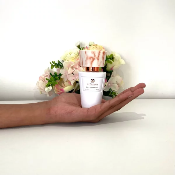 Flacon de parfum Olfazeta Extrait de Parfum 70 ml tenu dans une main devant un fond floral, illustrant la taille réelle du produit