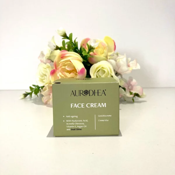 Crème visage anti-âge Aurodhea enrichie en acide hyaluronique, vitamine E, huile d'argan et bave d'escargot, présentée devant un fond floral